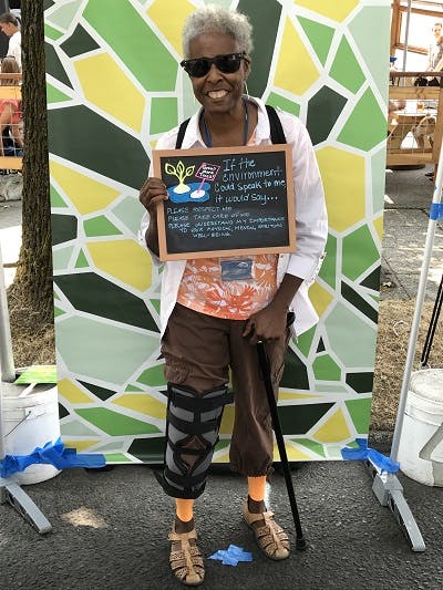 Elderly black woman holding a sign that reads "If the environment could speak to me, it would say..."