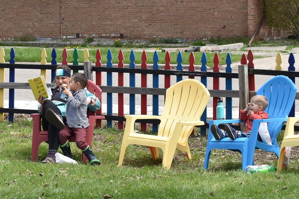 Lansing, MI, Pop-Up Park - a woman sitting on a read chair reading a book to a kid, another kid sitting on a blue chair