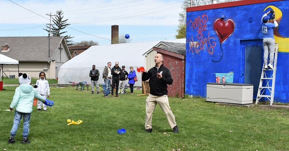 Lansing, MI, Pop-Up Park - man playing ball with kids, man in a realtor blue shirt on a ladder painting wall in the background