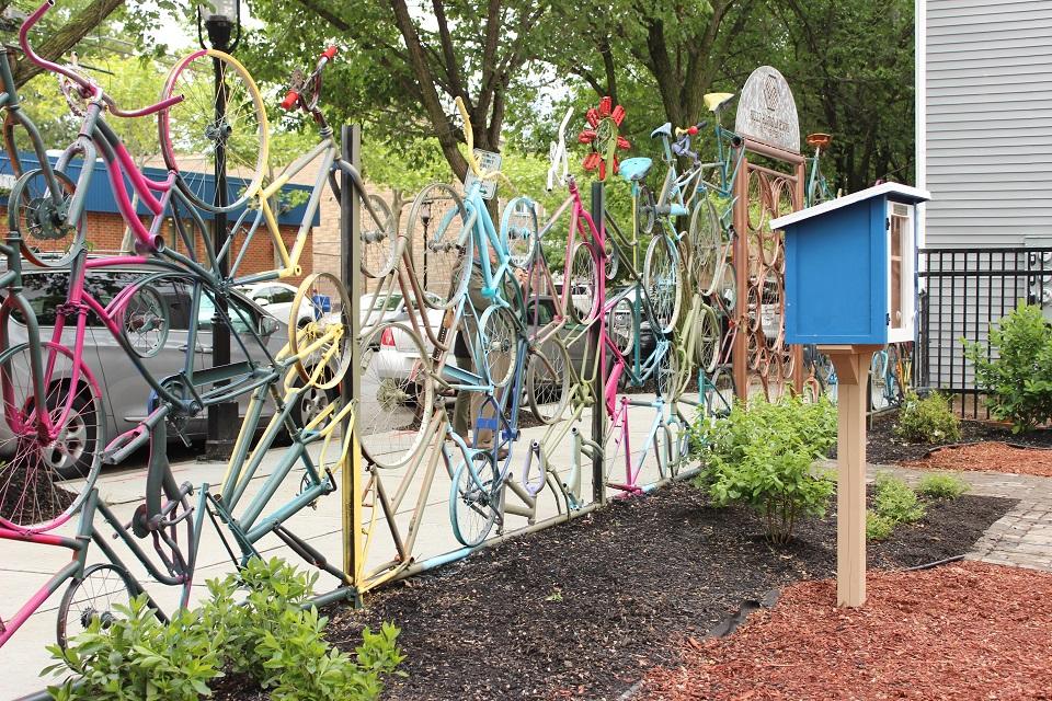 A fence made of colorful bicycle parts with the little library featured in the background.