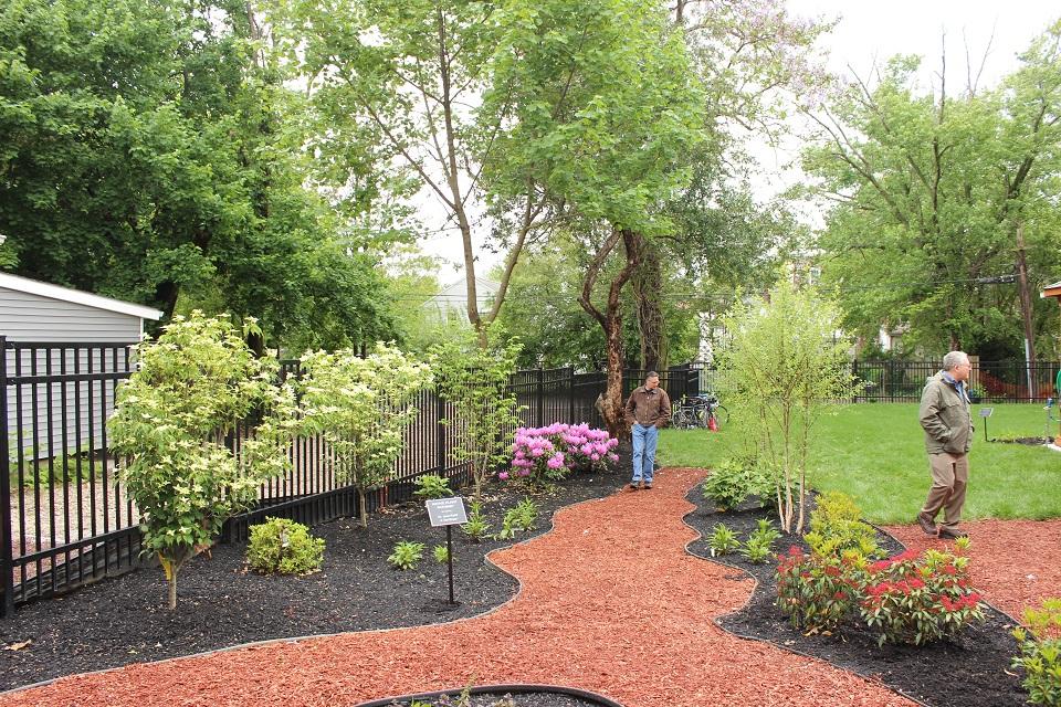 Two men walking in a mulch pathway surrounded by trees and plants in the Boys and Girls Club's garden.