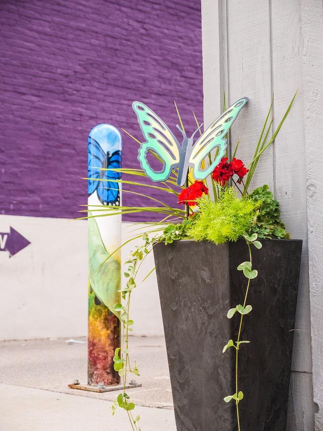 A plant vase featuring a green butterfly artwork with a purple mural in the background - Lebanon, Indiana.