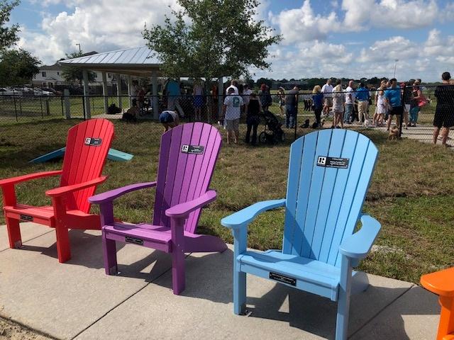 Melbourne, FL dog park - 3 multi-colored chairs, people with their dogs in the background