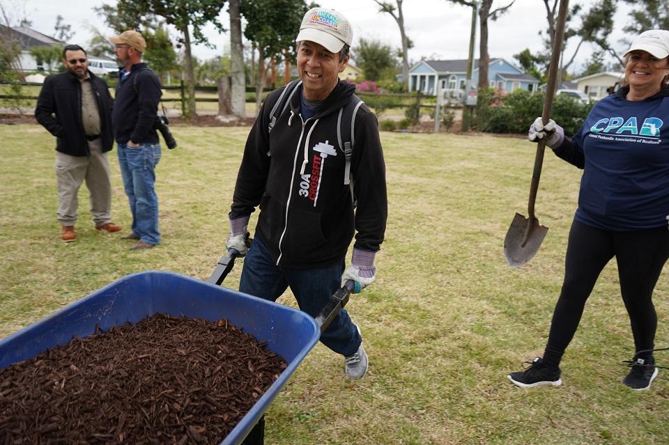 A REALTOR® volunteer pushing a wheelbarrow full of mulch during the Adams Park workday restoration, Panama City, FL