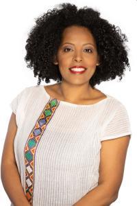 smiling black woman with curly hair in a white shirt with vertical strip of geometric pattern