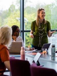 Three women around a conference table with reusable water bottles and greenery