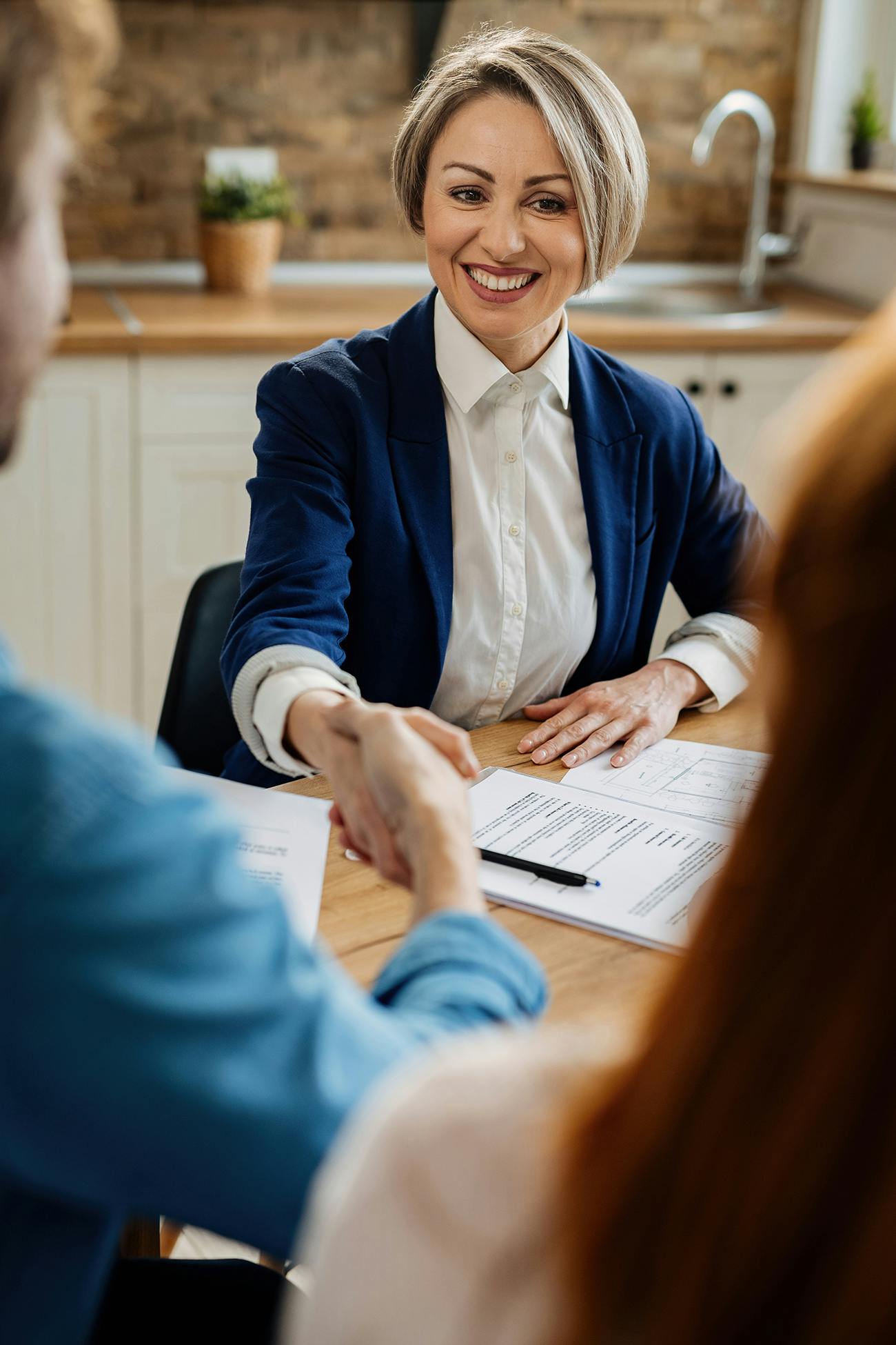 Woman in suit at table with clients shaking hands