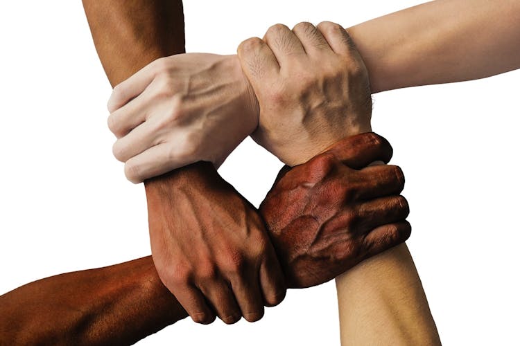 Four arms from four different people of different racial backgrounds holding each other's pulse representing unity and diversity