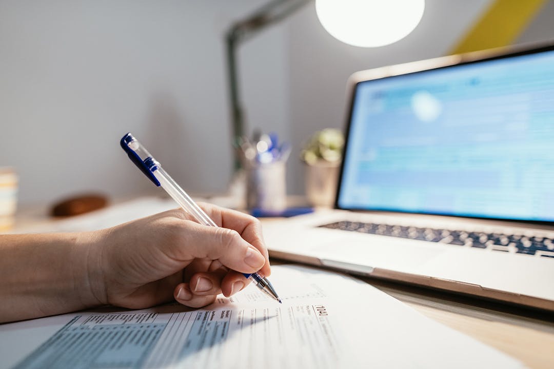 Hand with pen filling out form by laptop