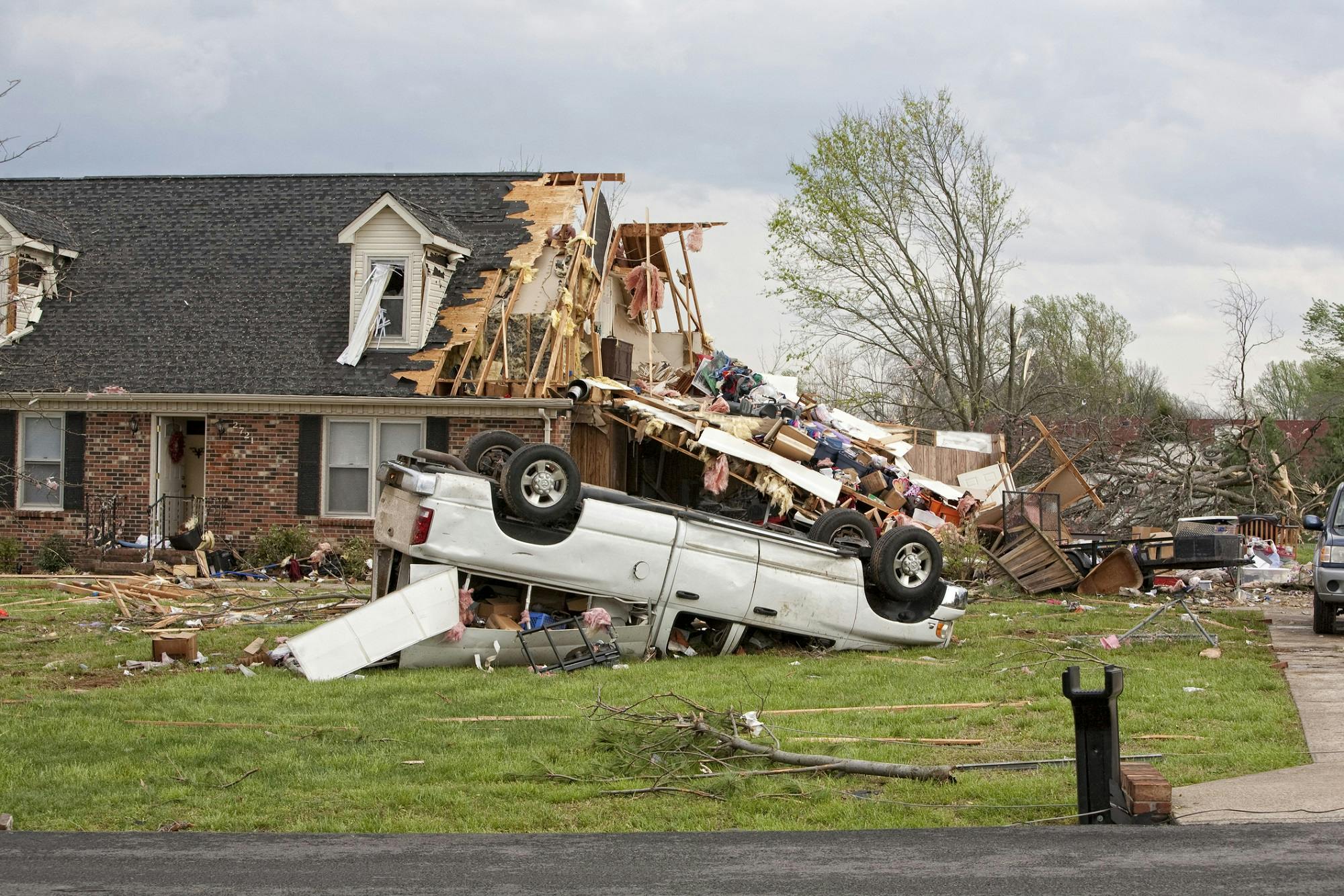 A house destroyed by a tornado featuring a pick-up truck upside down in its front yard