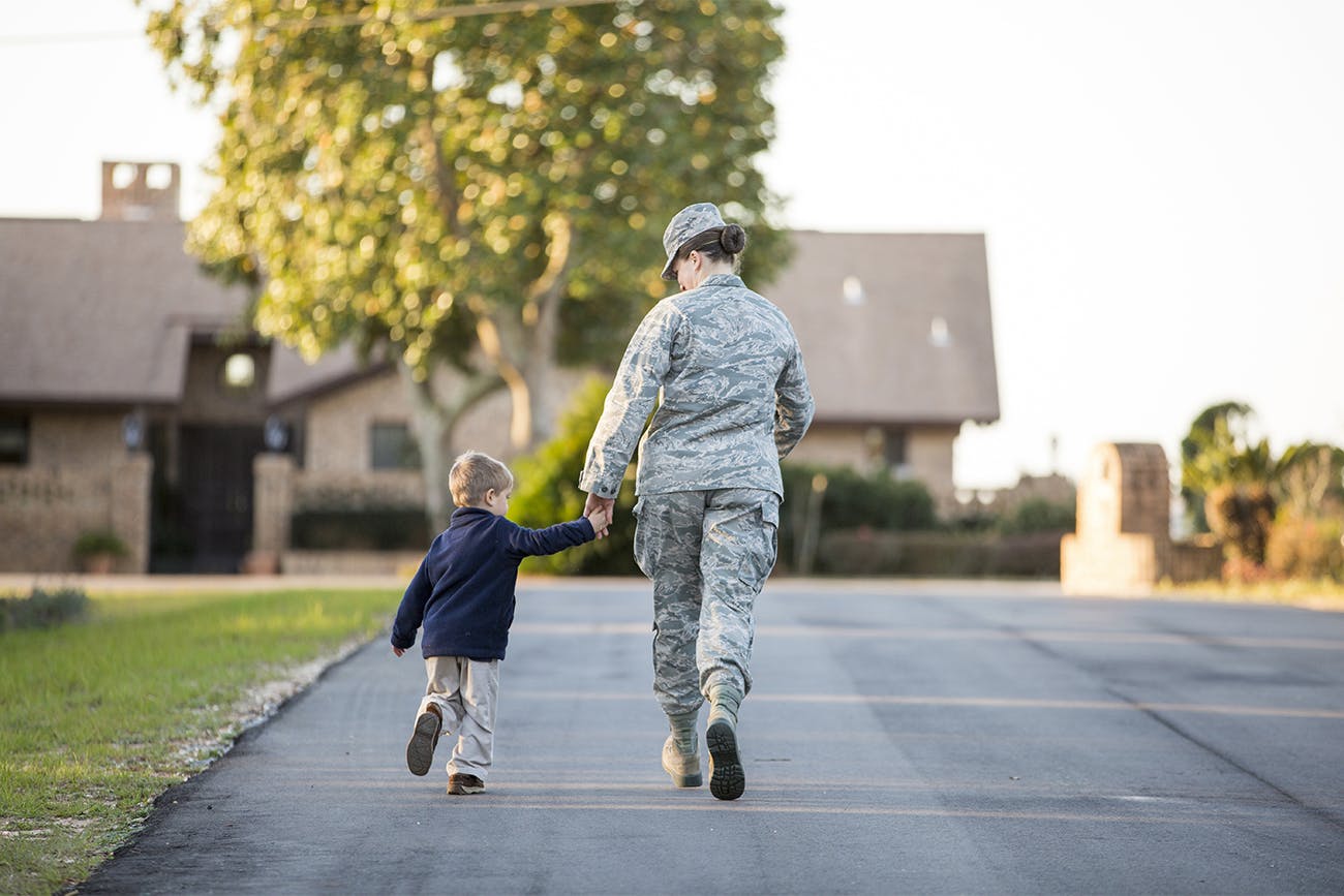 Woman in military fatigues and child walking toward house