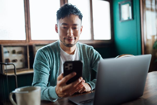 Man with laptop looking at smartphone