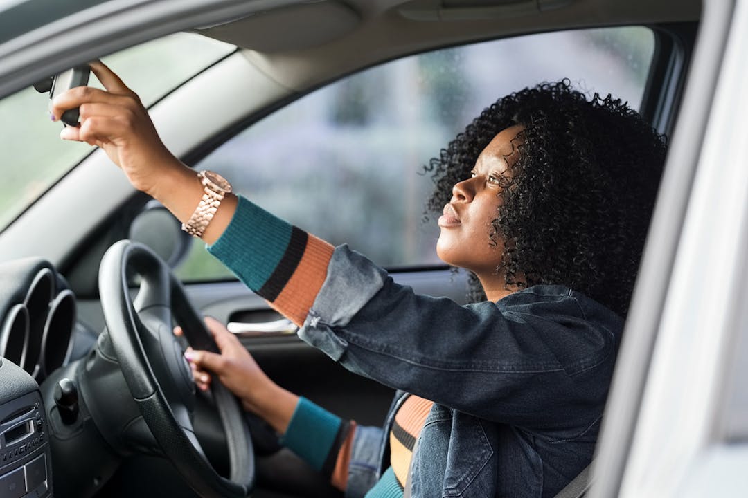 Woman sitting in driving seat adjusting rear view mirror