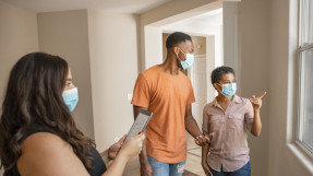 real estate agent showing man and woman an available property in masks