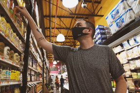 Man wearing a mask in a grocery store reaching the shelf