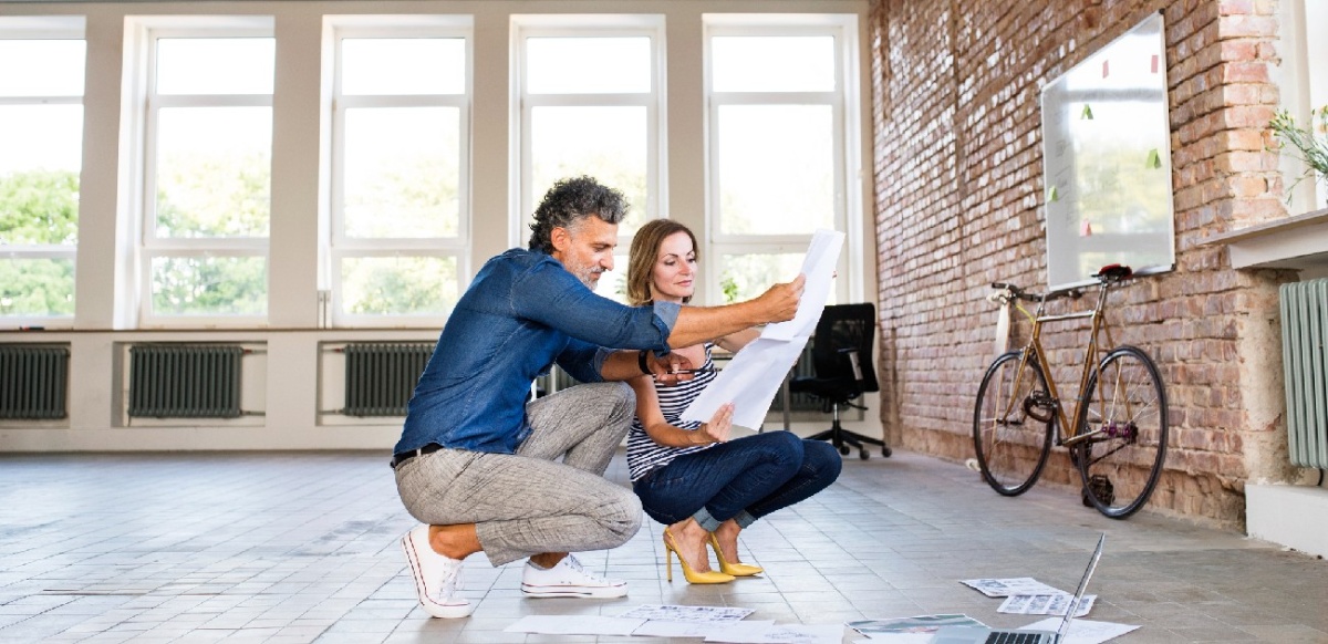 A man and a woman crouching down reviewing plans for an office space to be turned into an apartment.