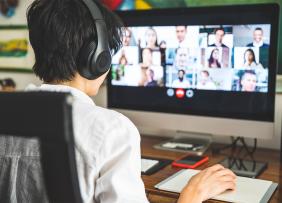 Person wearing headphones and watching a conference call on a computer